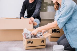 Dos personas realizando una mudanza. Se encuentran utilizando materiales y técnicas de embalaje, como por ejemplo embalando objetos frágiles en papel de diario.